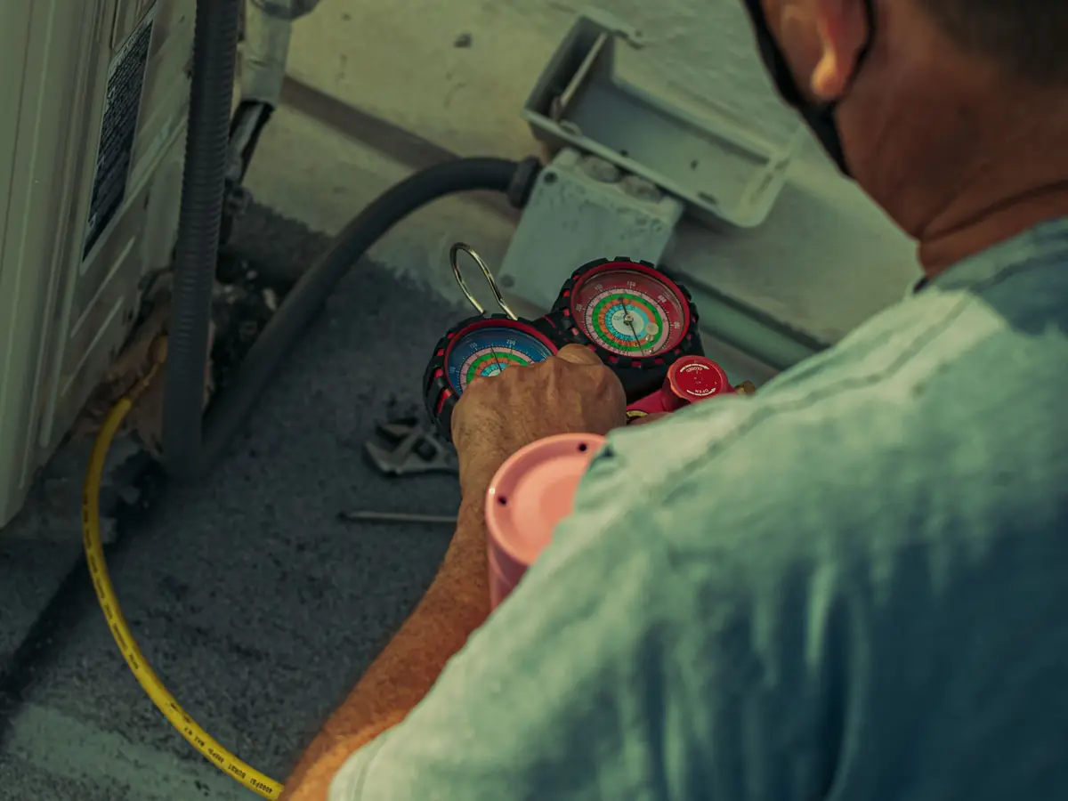 Technician repairing an outdoor air conditioning unit with gauges and tools