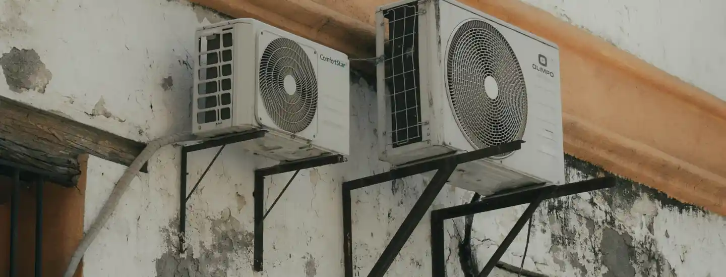 Two outdoor air conditioning units installed on a concrete wall