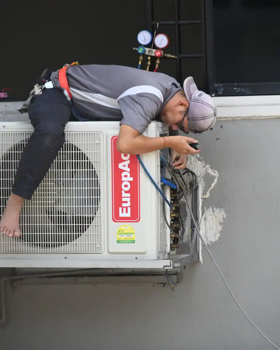 Technician working on an outdoor air conditioning unit mounted on a building wall