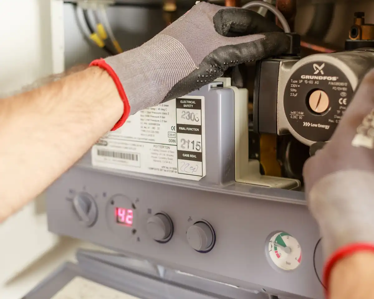 Gloved hands servicing a home heating boiler pump and controls
