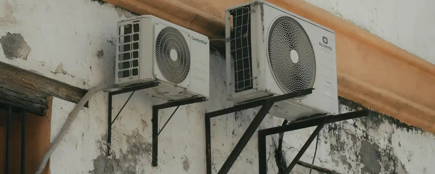 Two outdoor air conditioning units installed on a concrete wall