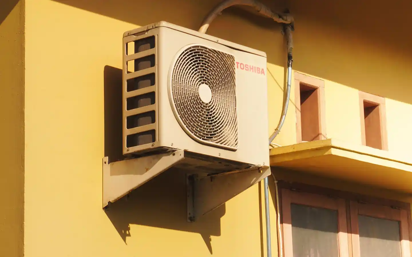 Outdoor air conditioner mounted on a sunny yellow wall