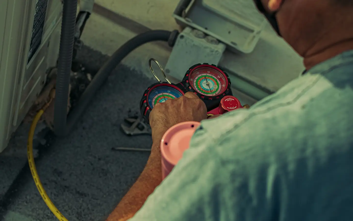 Technician repairing an outdoor air conditioning unit with gauges and tools